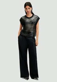 Top corto a maniche corte nero con design trasparente, abbinato a pantaloni neri a gamba larga. Il modello indossa tacchi a punta lucidi.
