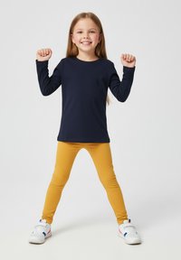 Granatowa bluzka z długim rękawem w połączeniu z żółtymi legginsami. Strój cechuje się prostym wzorem i jednolitymi kolorami, uzupełniony białymi trampkami.