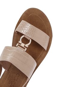 Nude faux leather sandal with two wide straps, one featuring a shiny silver buckle. Soft brown insole with stitched details. Flat design.