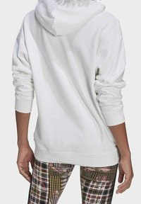 Vit hoodie med avslappnad passform, som har en stor huva och ribbade manschetter, kombinerad med mönstrade leggings i olika färger och texturer.