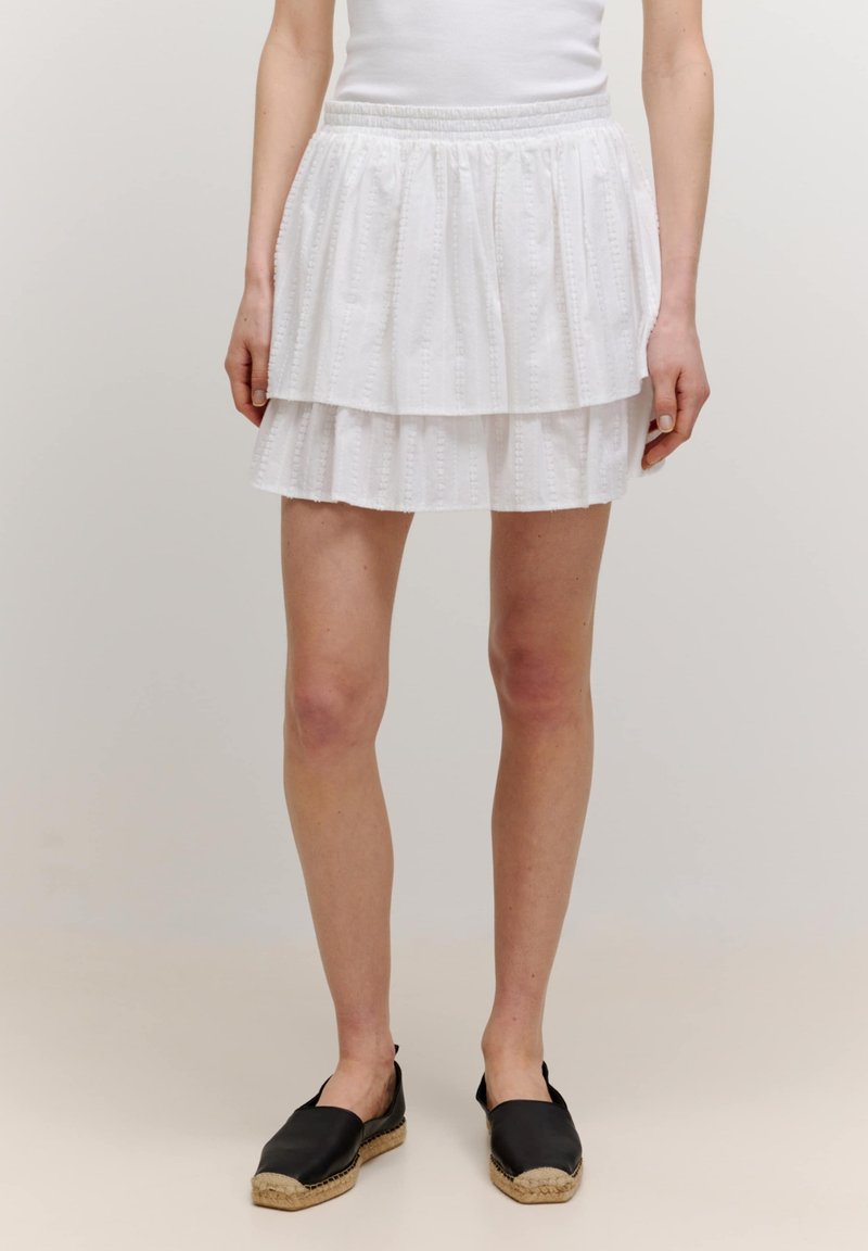 Witte gelaagde rok met een textuurontwerp, met twee lagen en een elastische tailleband. Gepaarde met zwarte espadrille instappers.