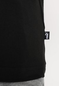 Musta puuvillainen T-paita, jossa on sivusaumassa "PUMA"-brändäyslappu. Kangas on sileäpintainen ja istuu vartalolle.