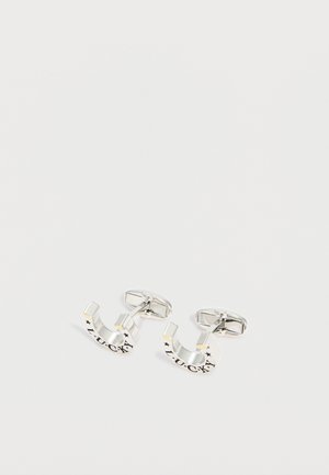 Hõbedased naelrehakujulised mansetinööbid, millele on graveeritud sõna "ÕNN" ning millel on väiksed tähedetailid, valgel taustal.