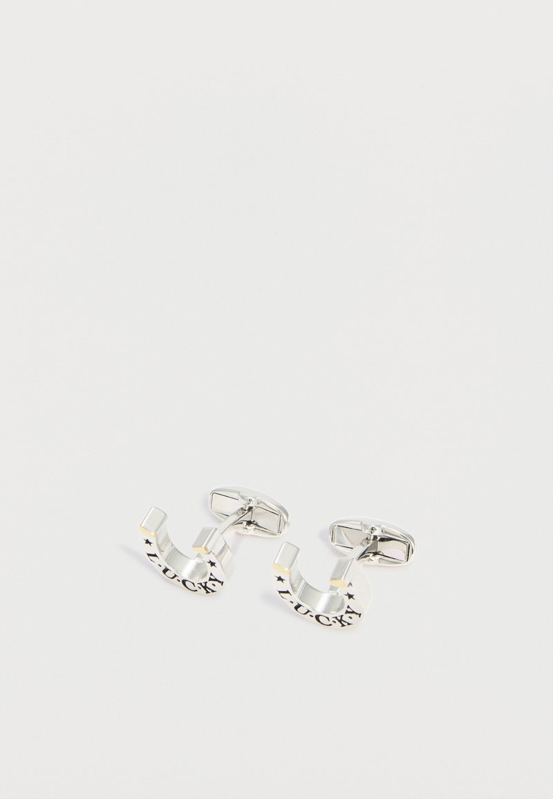 Ζευγάρι ασημένιων μανικετόκουμπων σε σχήμα πετάλου με τη λέξη "LUCKY" χαραγμένη και μικρές λεπτομέρειες αστέρια σε απλό λευκό φόντο.