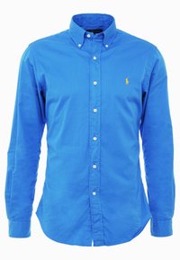 Jasnoniebieska koszula zapinana na guziki z długim rękawem, z kołnierzykiem zapinanym na guziki i małym żółtym haftowanym logo po lewej stronie klatki piersiowej.