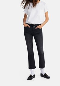 Svarta högmidjade jeans med rak benmodell, parat med en vit t-shirt med uppvikt ärm och svarta loafers med guldfärgade detaljer.