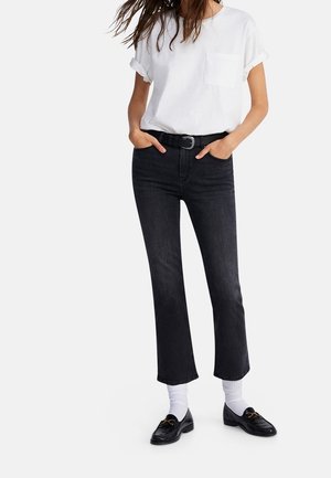 Jeans neri a vita alta con taglio dritto, abbinati a una maglietta bianca con maniche arrotolate e mocassini neri con dettagli in metallo dorato.