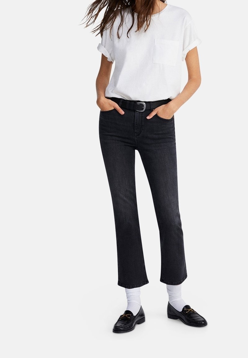 Svarta högmidjade jeans med rak benmodell, parat med en vit t-shirt med uppvikt ärm och svarta loafers med guldfärgade detaljer.