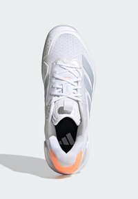 Bílá sportovní obuv s svrchní částí z síťoviny, šedými pruhy, oranžovým detailem na patě a texturovanou podrážkou. Má tkaničky a polstrovaný límec.