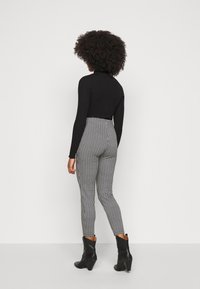 Svart långärmad topp med figursydd silhuett, kombinerad med högmidjade leggings med ett svart och vitt hundtandsmönster. Svarta ankelstövlar.