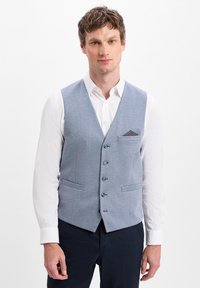 Helles blaues Weste mit einem strukturierten Muster, fünf Knöpfen und zwei vorderen Taschen, getragen über einem weißen Hemd, kombiniert mit dunklen Hosen.