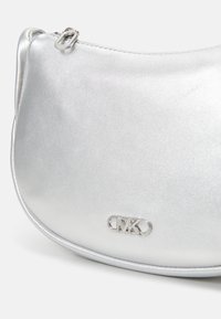 Borsetta a tracolla in metallo argento con forma arrotondata, caratterizzata da una texture liscia e un accento con logo sul davanti. Chiusura con zip sulla parte superiore.