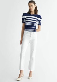 Top a righe navy e bianche con maniche a sbuffo e scollatura adornata di perle, abbinato a jeans bianchi a campana con bottoni e sandali con tacco color crema.
