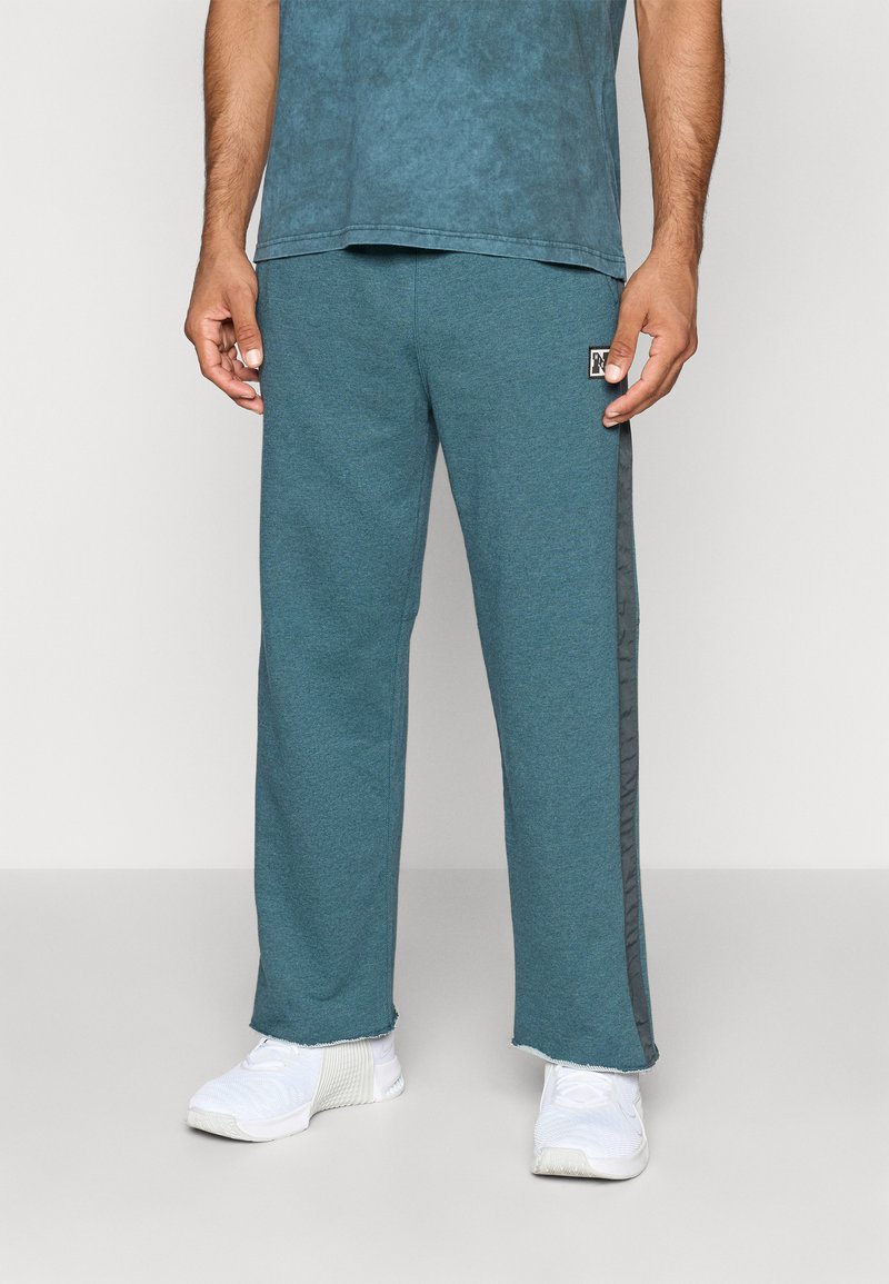 Teal sweatpants med afslappet pasform, med grå striber på siden og et mærketegn på låret. Fremstillet af blødt, tekstureret stof.