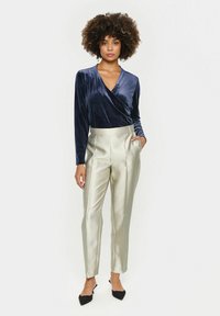Navy velvet wrap top with long sleeves paired with light metallic silver tailored trousers and black pointed-toe heels.