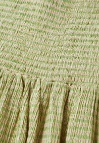 Tissu rayé vert et beige avec un design texturé et froncé. Le matériau est léger avec une finition douce et froissée.
