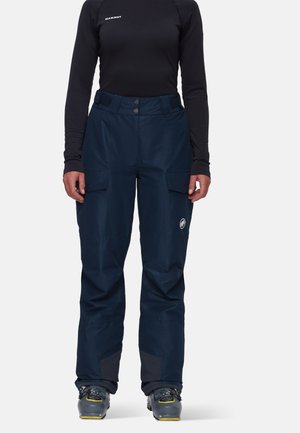 Navy blue waterproof ski pants with a high waist, two front pockets, reinforced cuffs, and an emblem on the left thigh. Smooth texture.