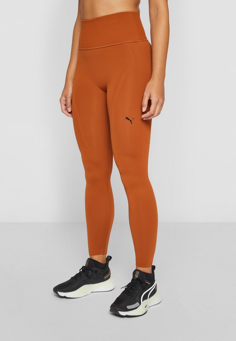 Leggings arancioni vivaci con vita alta e tessuto elasticizzato, con un logo Puma nero sul lato sinistro e una texture liscia.