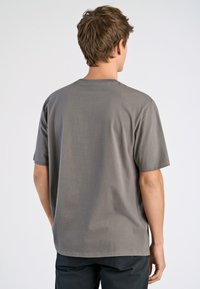 T-shirt gris à manches courtes en tissu doux, avec un col rond et une coupe décontractée, présentant un dos uni sans logos visibles.
