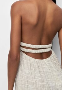 Rückenfrei mit zwei strukturierten weißen Riemen, die quer verlaufen, getragen zu einem leichten, plissierten, strukturierten Rock oder Kleid.
