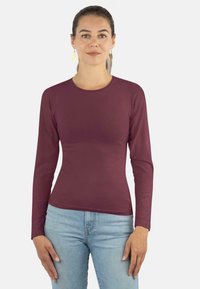 Langärmeliges kastanienbraunes Oberteil aus glattem Stoff mit Rundhalsausschnitt und taillierter Silhouette, kombiniert mit hellblauen Jeans.