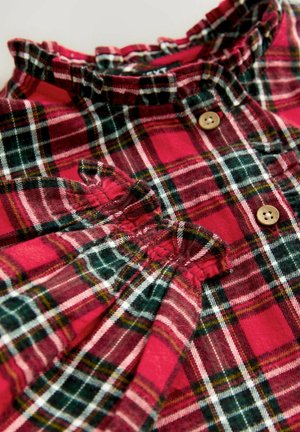 Camicia a quadri rossi e verdi con colletto arricciato, bottoni in legno e dettagli di tessuto arricciato. Materiale in cotone texturizzato.