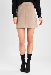 Minifalda de ante en beige con un diseño ajustado, que presenta una costura central y una textura suave, combinada con botas de tacón negras.