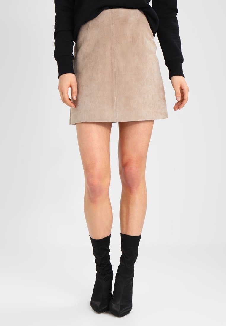 Minifalda de ante en beige con un diseño ajustado, que presenta una costura central y una textura suave, combinada con botas de tacón negras.