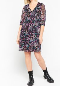 Svart klänning med ett paisleymönster i rosa, blått och vitt. Har en V-ringning och trekvartslånga ärmar. Bärs med svarta ankelboots.