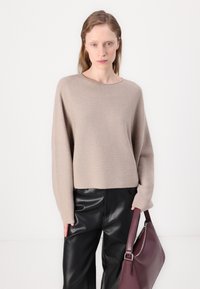 Beige, oversized kötött pulcsi széles kivágással és hosszú ujjakra, fekete bőr nadrággal és bordó táskával párosítva. Simább textúra.