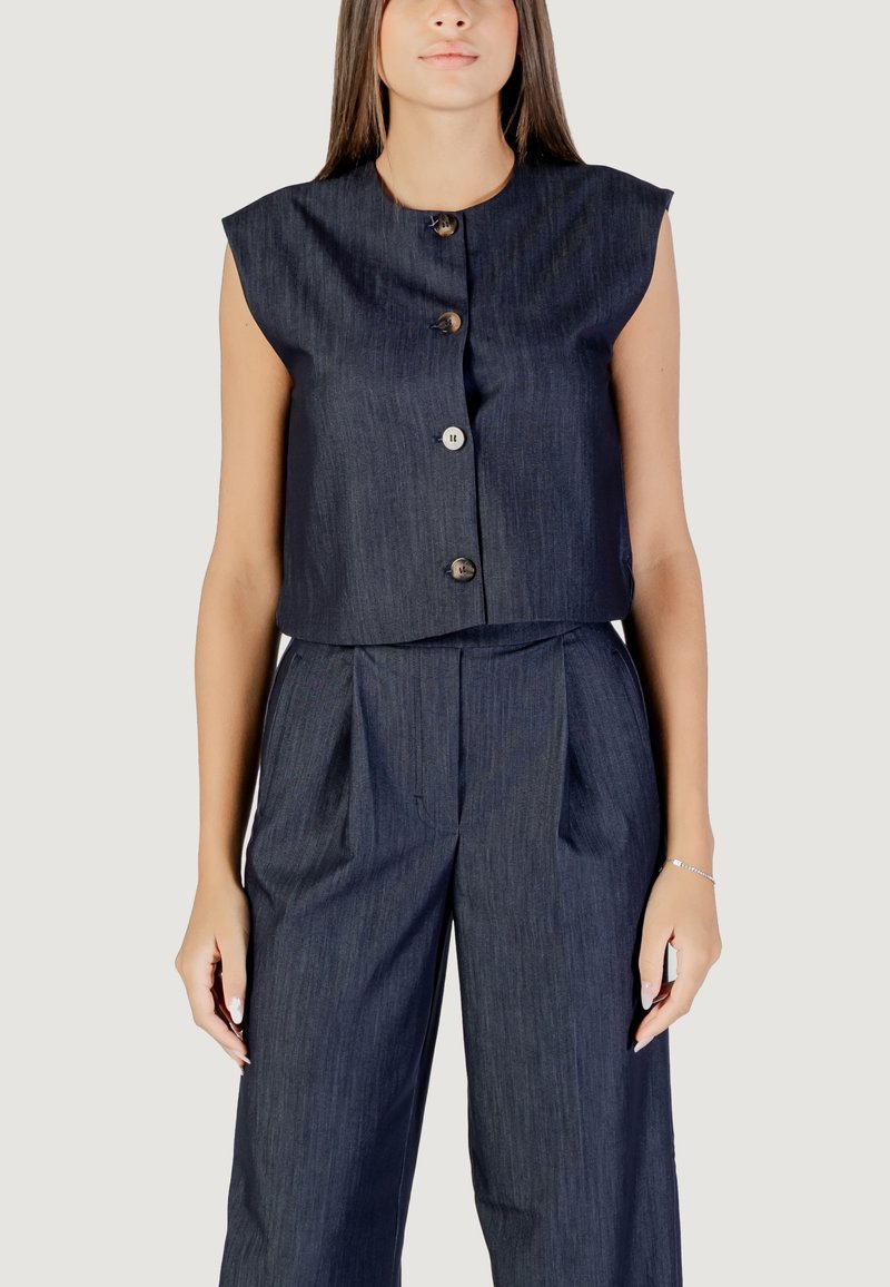 Giubbotto corto blu navy con maniche corte, caratterizzato da un'apertura a bottoni. Abbinato a pantaloni a vita alta plissettati, entrambi in un tessuto simile al denim.