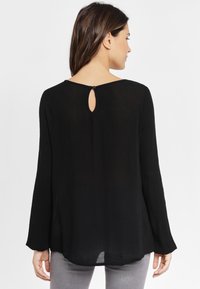Svart långärmad blus med detalj i nyckelhål på baksidan och avslappnad passform. Tillverkad i lätt tyg, med rundad halsringning och mjuk textur.