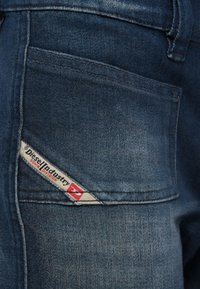 Kék farmerral hátsó zsebe, melyen egy fehér és piros Diesel Industry Denim Division feliratú címke van varrva a zseb sarkánál.