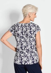 Bloemenpatroon top met korte mouwen, met een marineblauwe achtergrond en witte/paarse bloemen. Soepele textuur met een relaxed fit.