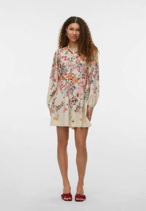 Floral dress in cream fabric with long sleeves, belted waist, and multicolored patterns of flowers. Paired with red floral sandals.