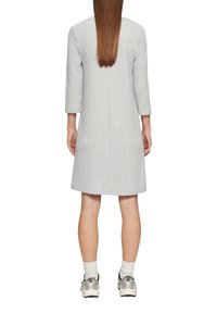 Graues, knielanges Kleid mit 3/4-Ärmeln; strukturiertes Material ohne Muster. Kombiniert mit weißen Socken und grauen Sneakers. Minimalistisches Design.