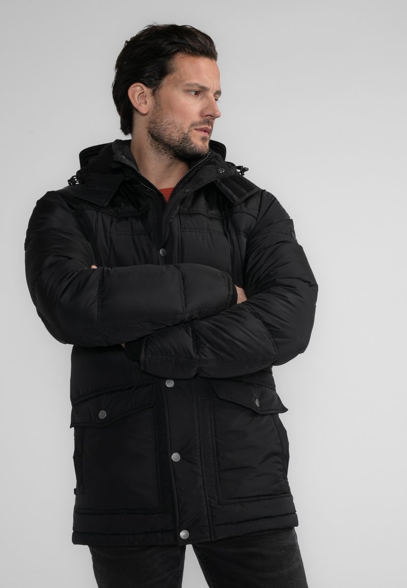 Černá bunda s péřovým vzhledem s kapucí, více předními kapsami, patentkami a hladkou texturou. Zpevněné švy podtrhují design.