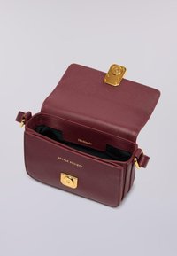 Borsa a tracolla in pelle bordeaux aperta con chiusura dorata, interno nero e lettering dorato "Gentle Society" e "Trussardi" all'interno.