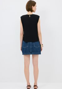 Schwarzes ärmelloses Oberteil mit einem Schlüssel-ausschnitt hinten, kombiniert mit einem Denim-Minirock mit zwei Rückentaschen und einem gesäumten Abschluss.