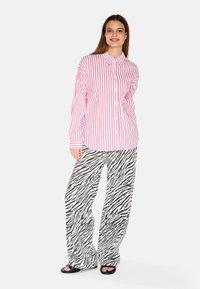 Pink and white striped button-up shirt with a collar, paired with loose black and white zebra-print trousers, and black slide sandals.