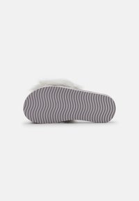 White plush slipper with a fluffy top, featuring a smooth sole with a wavy pattern for grip and comfort.