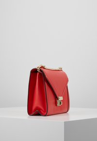 Rød læderhåndtaske med guldkæde-rem, tri-fold design, geometrisk lås og kontrastfarvet sort kant. Tekstureret overflade med blød glans.