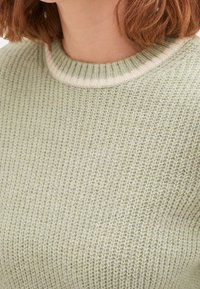 Maglione lavorato a maglia verde chiaro con un motivo testurizzato e un colletto a coste color crema. La vista ravvicinata mette in risalto il materiale e lo stile.