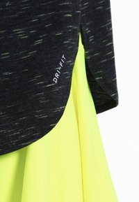 Zwart en groen Dri-Fit sporttopje met een afgeronde zoom, gecombineerd met een felgele gelaagde rok. Gladde textuur en modern ontwerp.