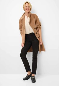 Lange, beige wollen jas met zwarte knopen, crèmekleurige blouse, zwarte slim fit broek en zwarte loafers met gouden accenten. Minimalistisch ontwerp, gladde textuur.