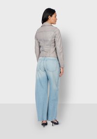 Giacca in pelle grigia con design aderente, cuciture sul retro e texture lineare, abbinata a jeans a gamba larga blu chiaro e tacchi blu navy.