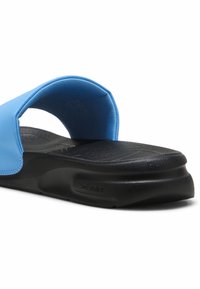 Blå skridsko sandal med en bred rem og sort tekstureret sål. Har letvægts skumsål med "Soft Ride" branding på siden.