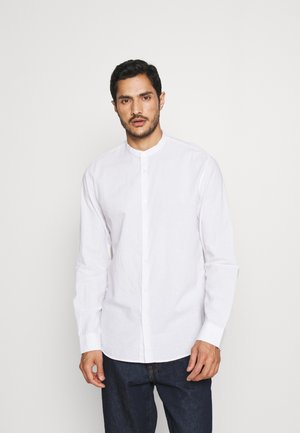 Camisa blanca de manga larga con cuello de banda, cierre frontal abotonado y tejido ligero. Combinada con jeans de mezclilla oscuros, mostrando una textura suave.