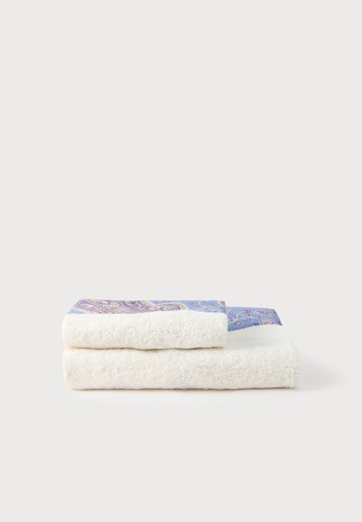 Deux serviettes blanches pliées empilées avec une bordure en tissu à motifs bleus et violets sur un fond blanc uni.