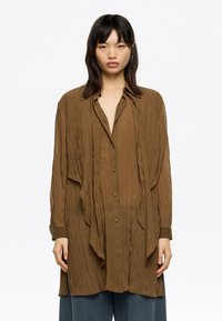 Brown textured button-up shirt with a draped design, long sleeves, and a collar. Slightly oversized with a relaxed fit.